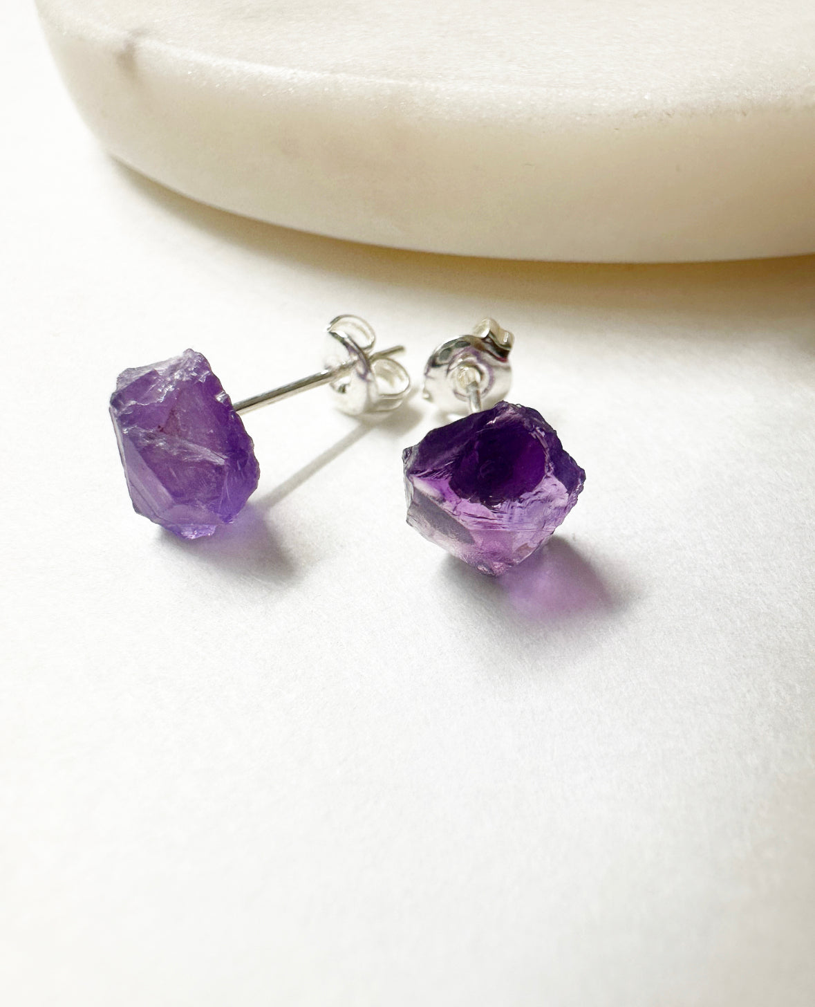Close-up view of raw amethyst stud earrings.