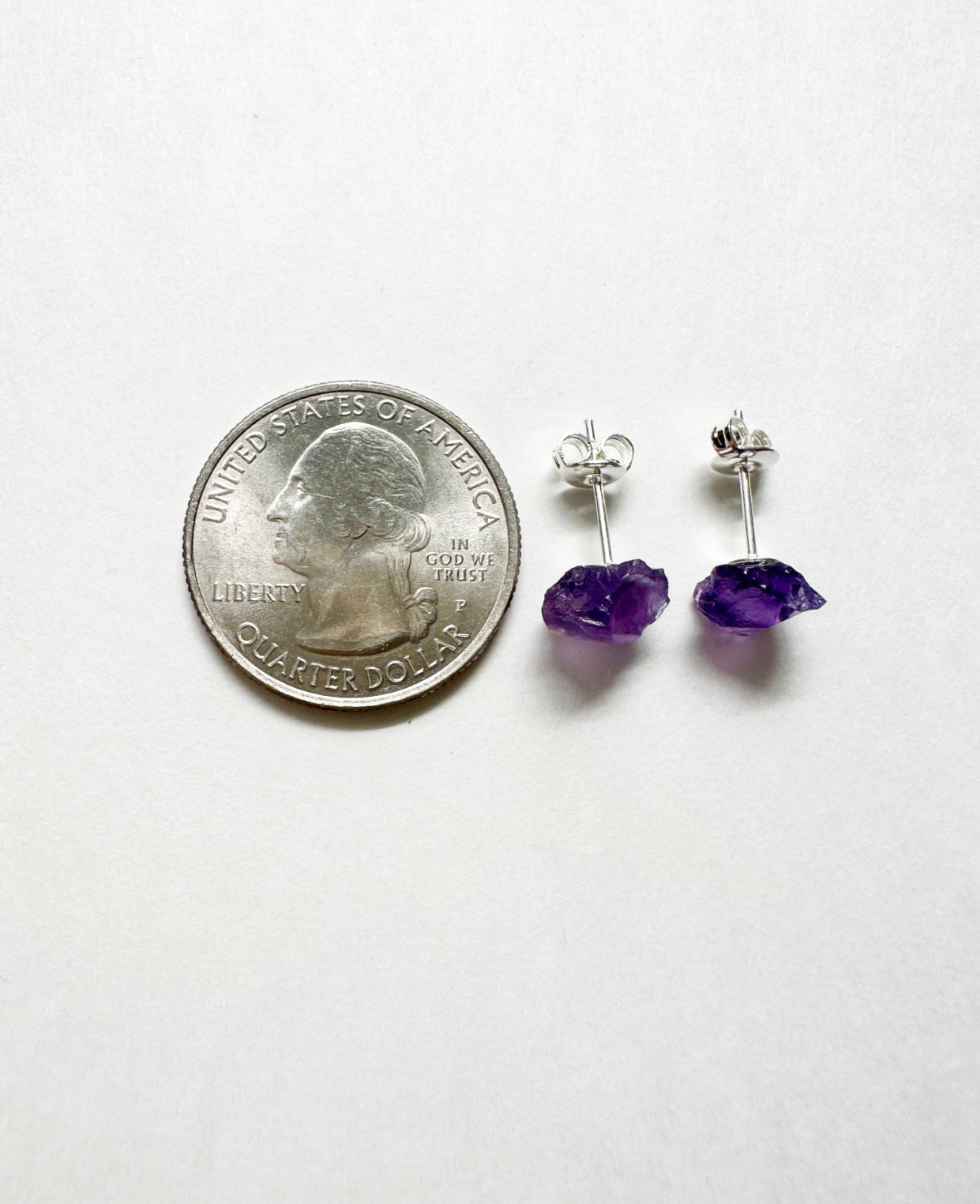 Raw amethyst stud earrings next to a quarter for size comparison.