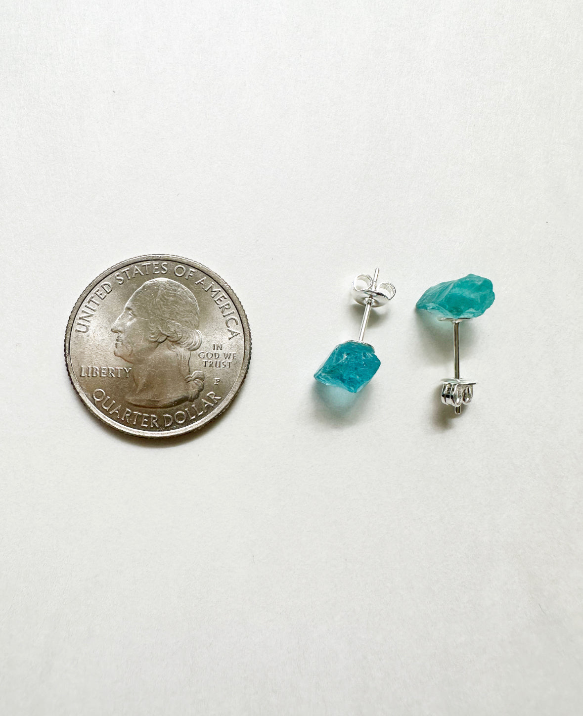 Raw aquamarine stud earrings next to a quarter for size comparison.