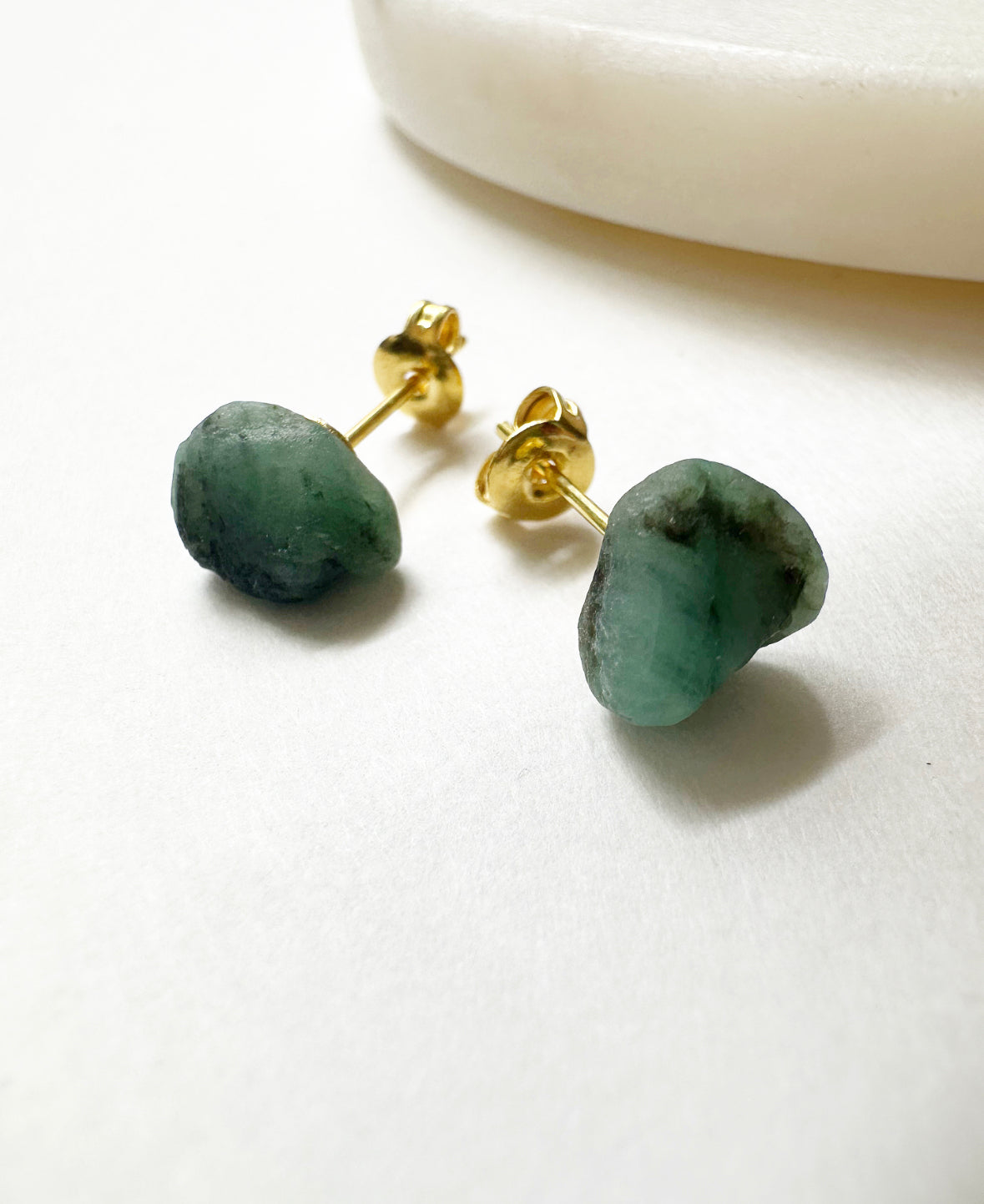 Close-up view of raw emerald stud earrings.