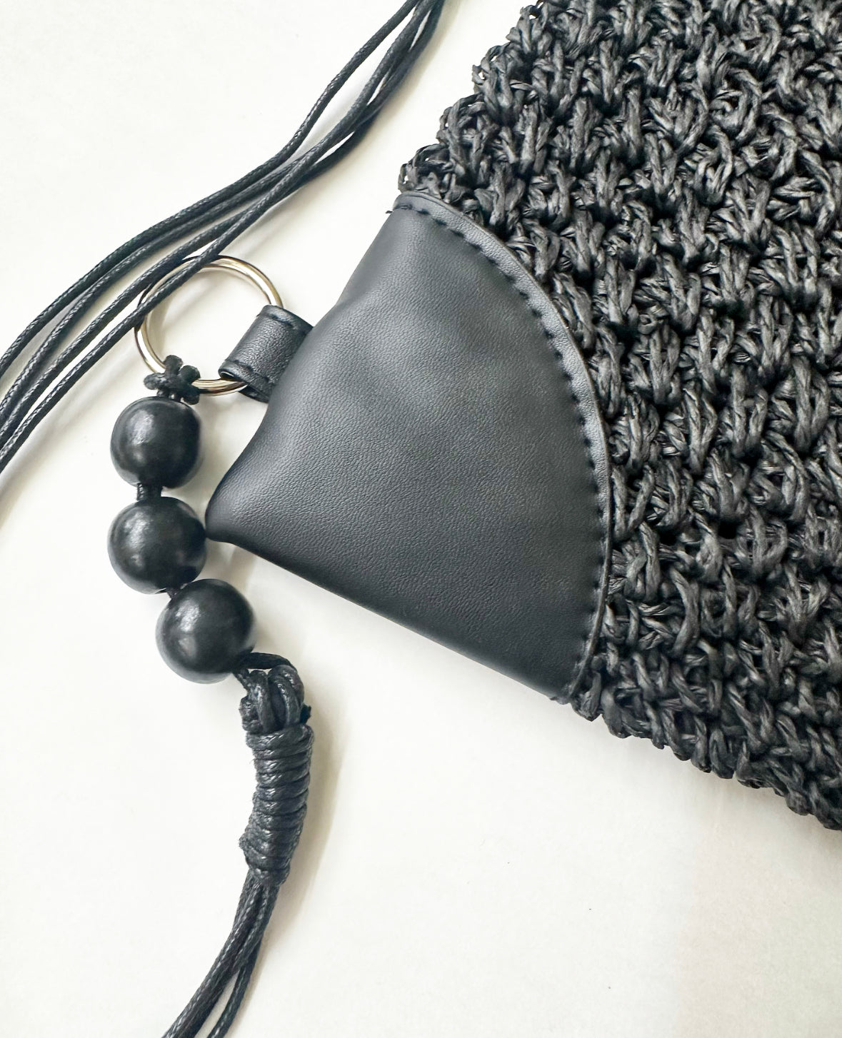 Close-up view of woven material, faux leather, and beading details on black bag.