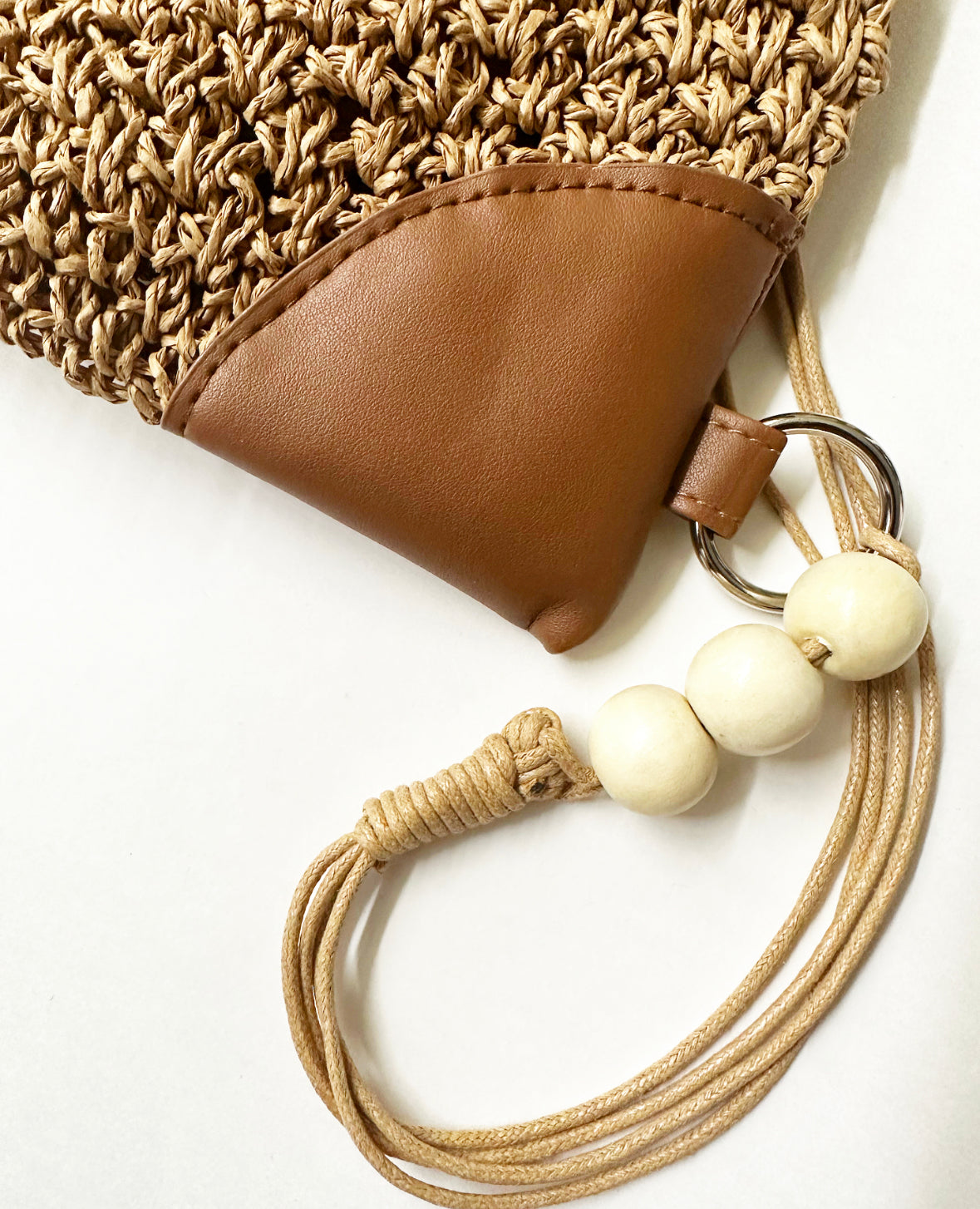 Close-up view of woven material, faux leather, and beading details on tan bag.