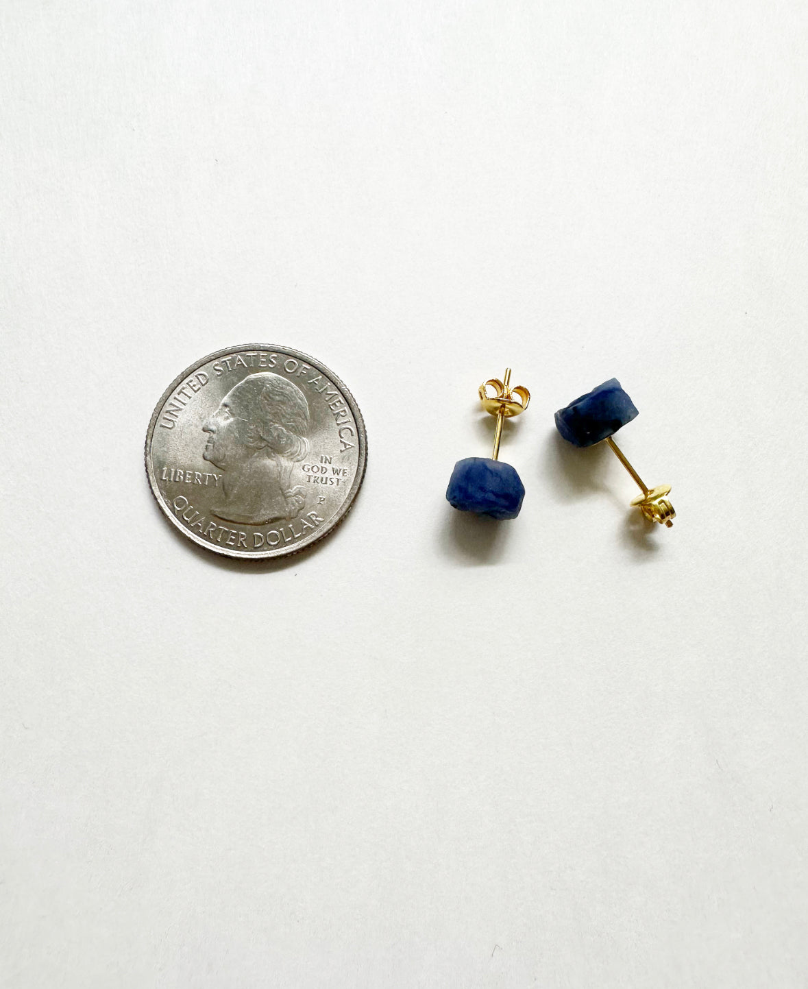 Raw sapphire stud earrings next to a quarter for size comparison.