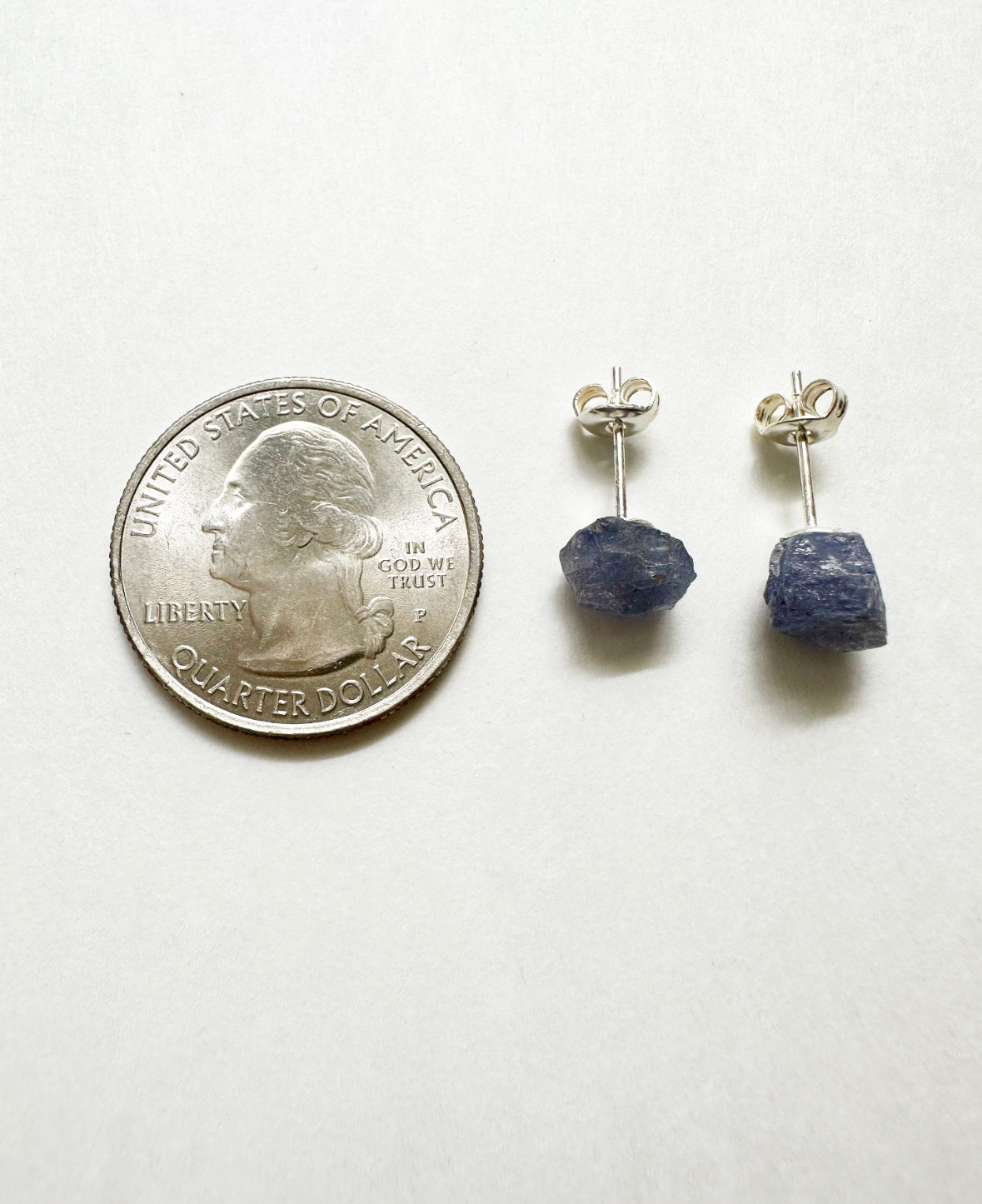 Raw tanzanite stud earrings next to a quarter for size comparison.