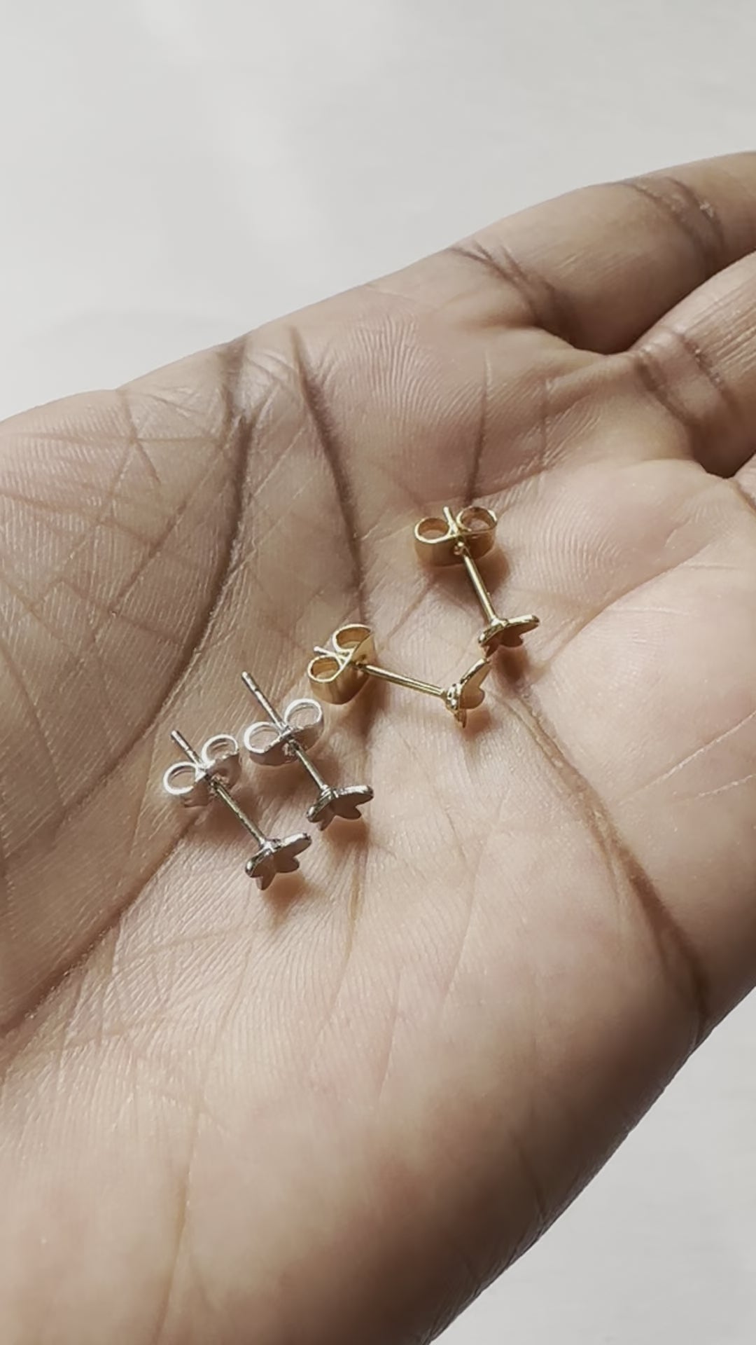 A real-time view of our Tiny Flutters Stud Earrings shown on the palm of model's hand.