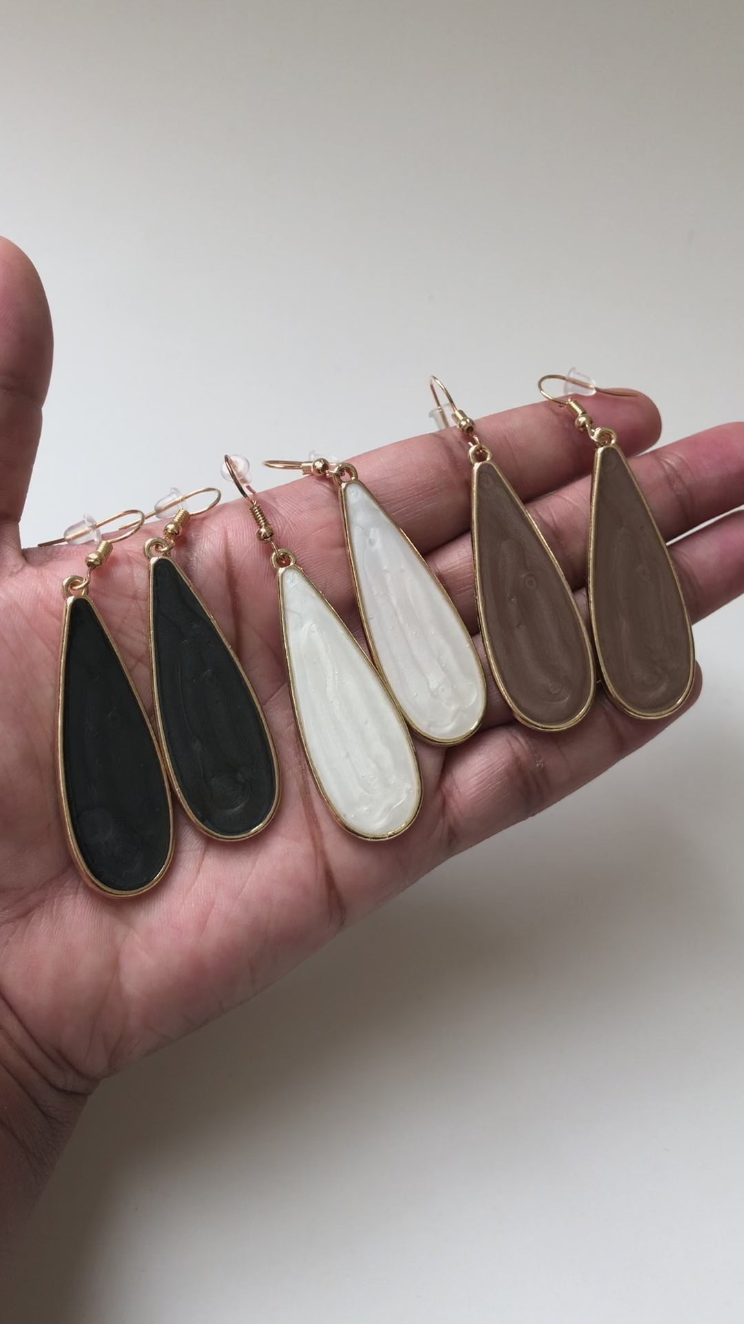 A real-time view of our Candy Rain Drop Earrings (Black, White, and Taupe) shown on the palm of model's hand.