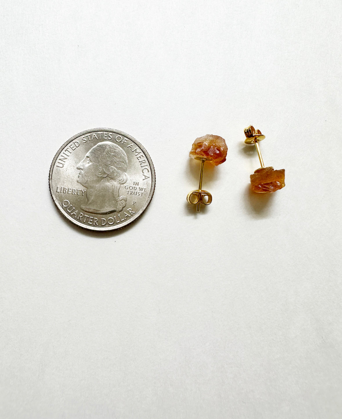 Raw citrine stud earrings next to a quarter for size comparison.