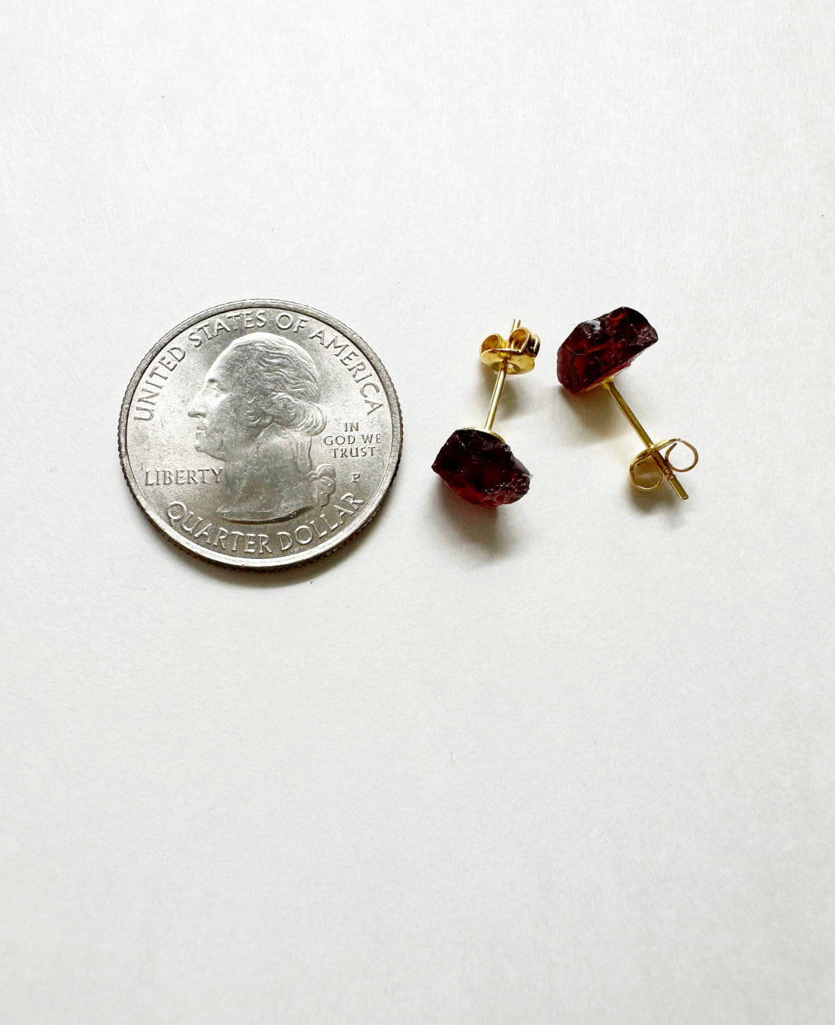 Raw garnet stud earrings next to a quarter for size comparison.