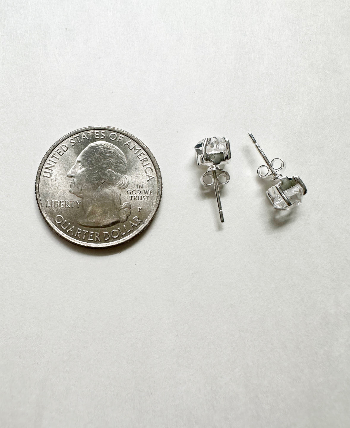 Herkimer diamond stud earrings next to a quarter for size comparison.