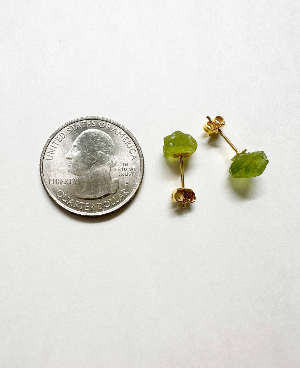 Raw peridot stud earrings next to a quarter for size comparison.