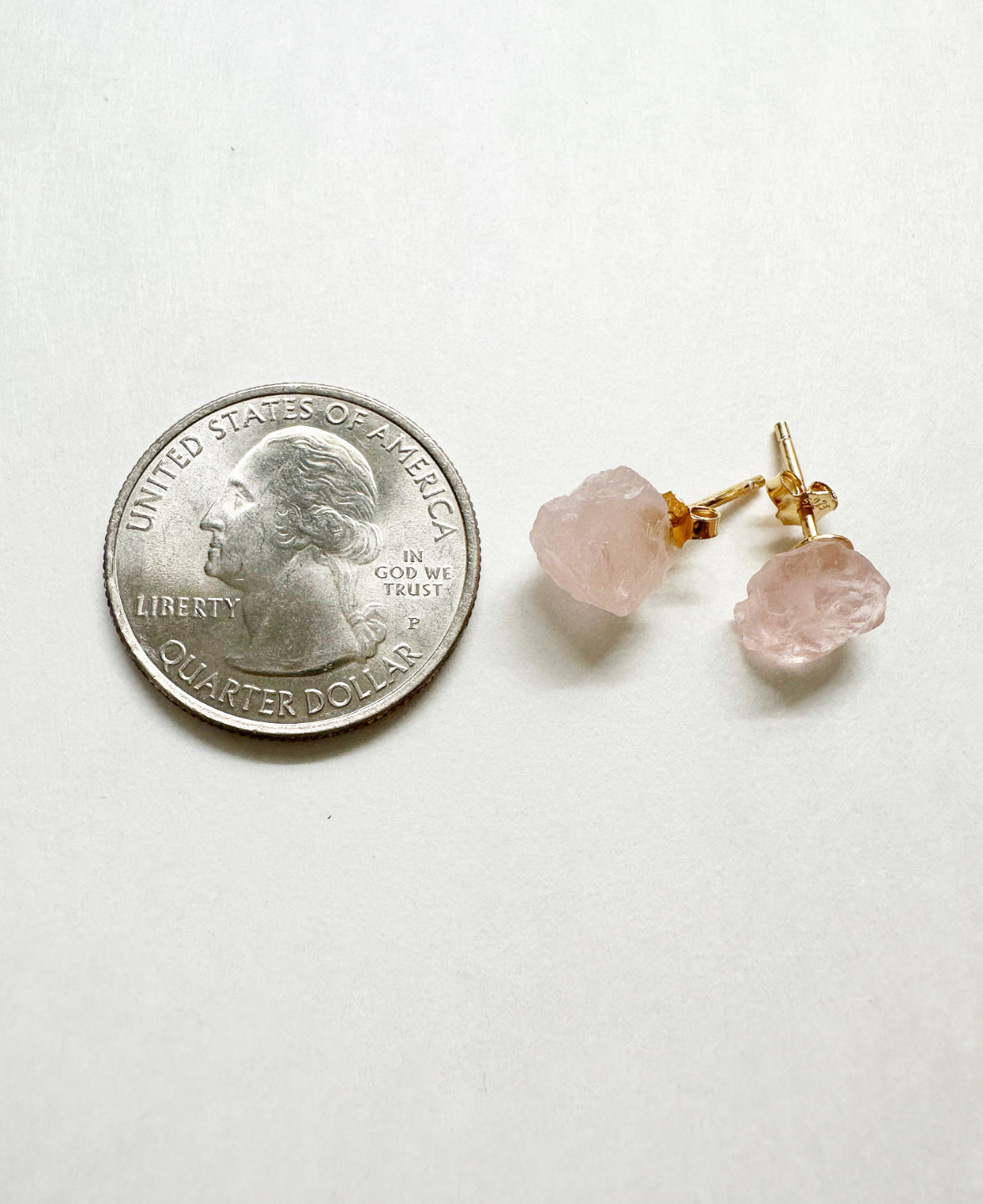 Raw rose quartz stud earrings next to a quarter for size comparison.